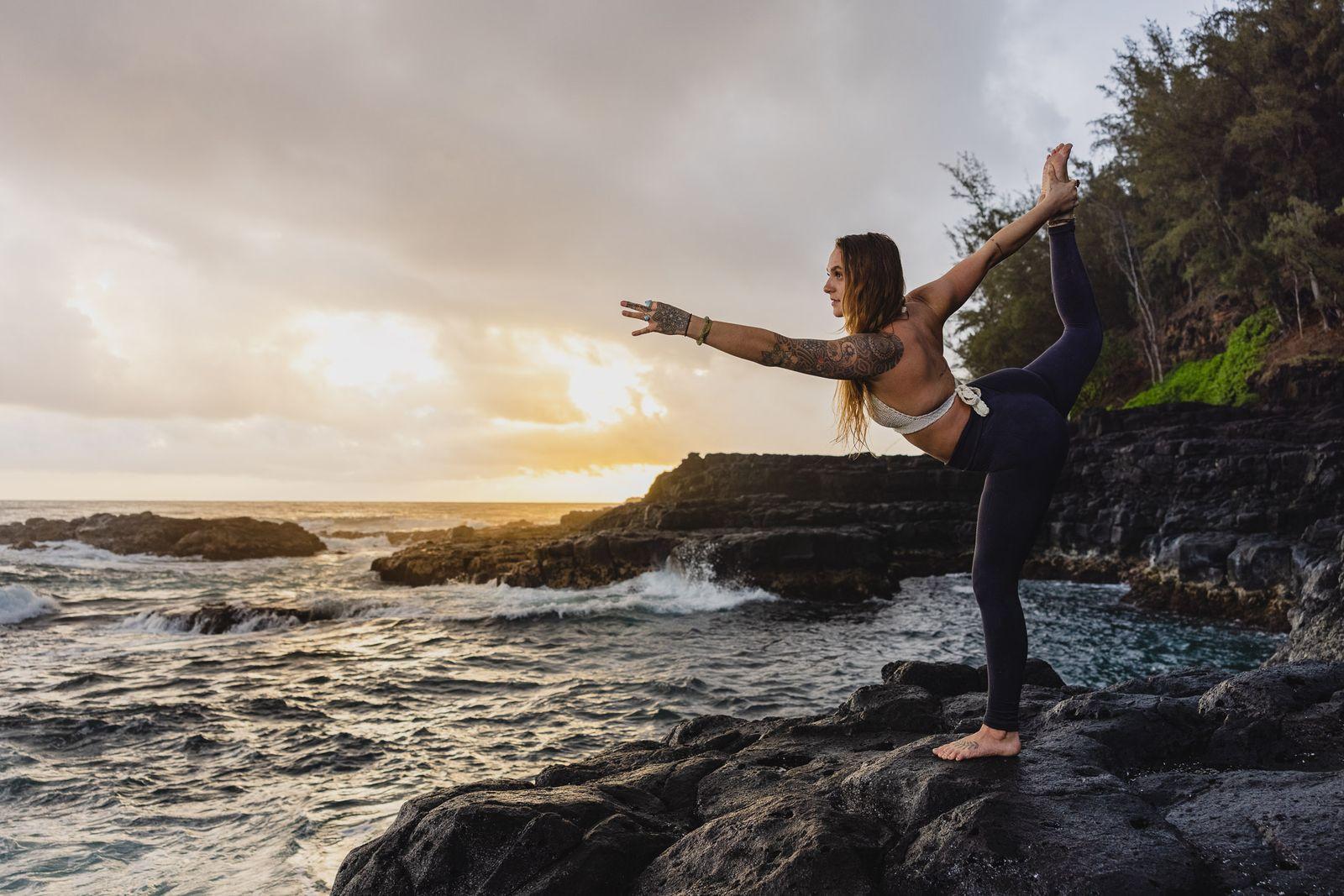 a woman doing a yoga pose on a rock near the ocean