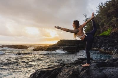 a woman doing a yoga pose on a rock near the ocean