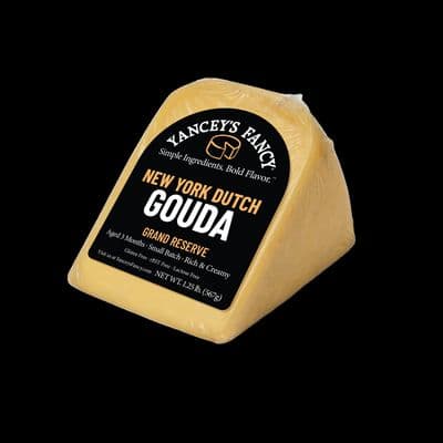 Studio product photo of a golden-yellow wax-wrapped wedge of New York Dutch Gouda cheese with a black label against a solid black background.