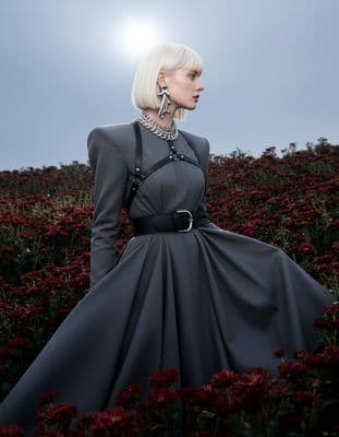 a woman in a gray dress standing in a field of flowers