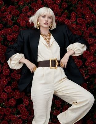 a woman with blonde hair wearing a black jacket and white pants