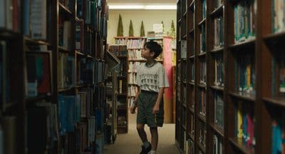 a young man standing in a library between rows of books