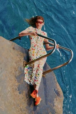 a woman in a colorful dress sitting on a rock next to the ocean