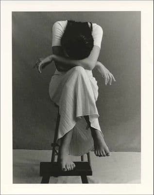 a black and white photo of a woman sitting on a stool