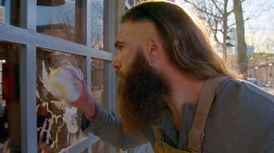 a man with long hair and a beard is looking through a window