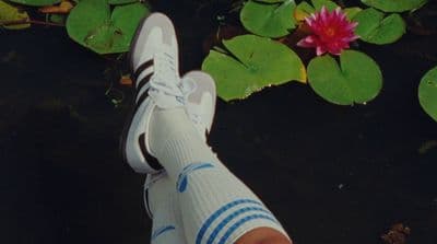 a person's feet in a pair of white shoes next to water lilies