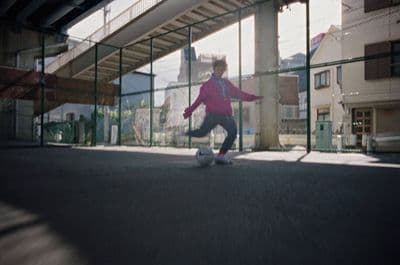 a young girl kicking a soccer ball under a bridge