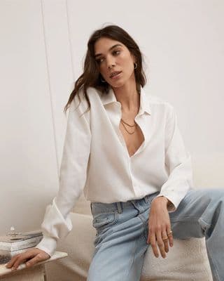a woman sitting on a couch wearing a white shirt and jeans