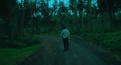 a man walking down a dirt road in the middle of a forest