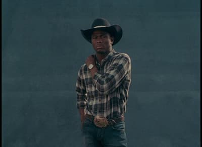 a man wearing a cowboy hat standing in front of a wall