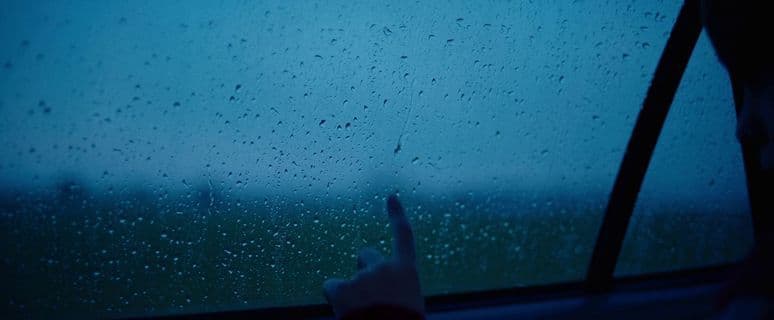 a person points at the rain outside of a window