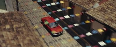 a red car driving down a street next to tall buildings
