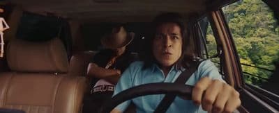 a man driving a car with another man behind him