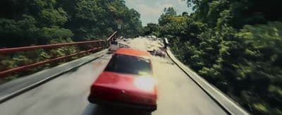 a red car driving down a road next to a forest