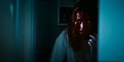 a man with long hair and red eyes in a dark room