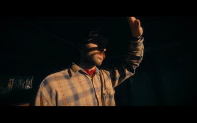 a man with a beard and glasses holding his hand up in the air