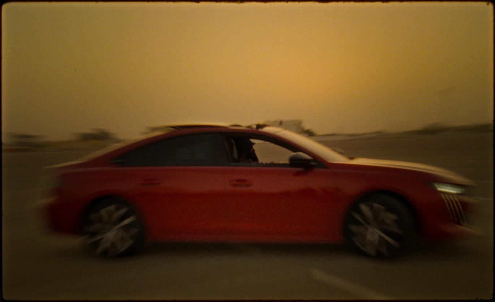 a red car driving down a street with a sky background
