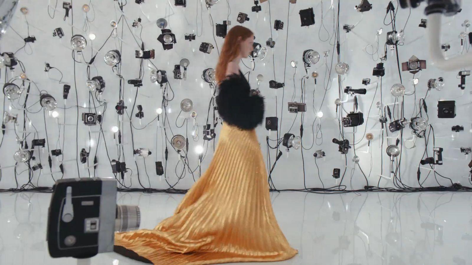 a woman in a yellow dress standing in front of a wall of wires