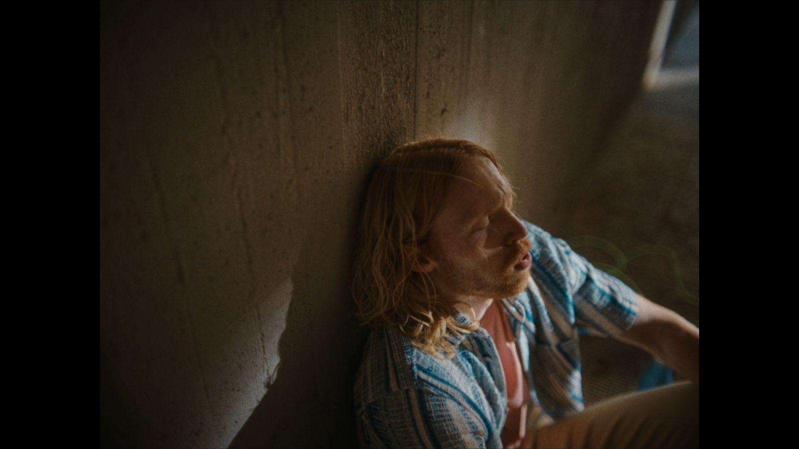 a man with long hair sitting against a wall
