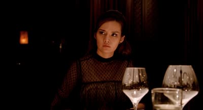 a woman sitting at a table with two wine glasses