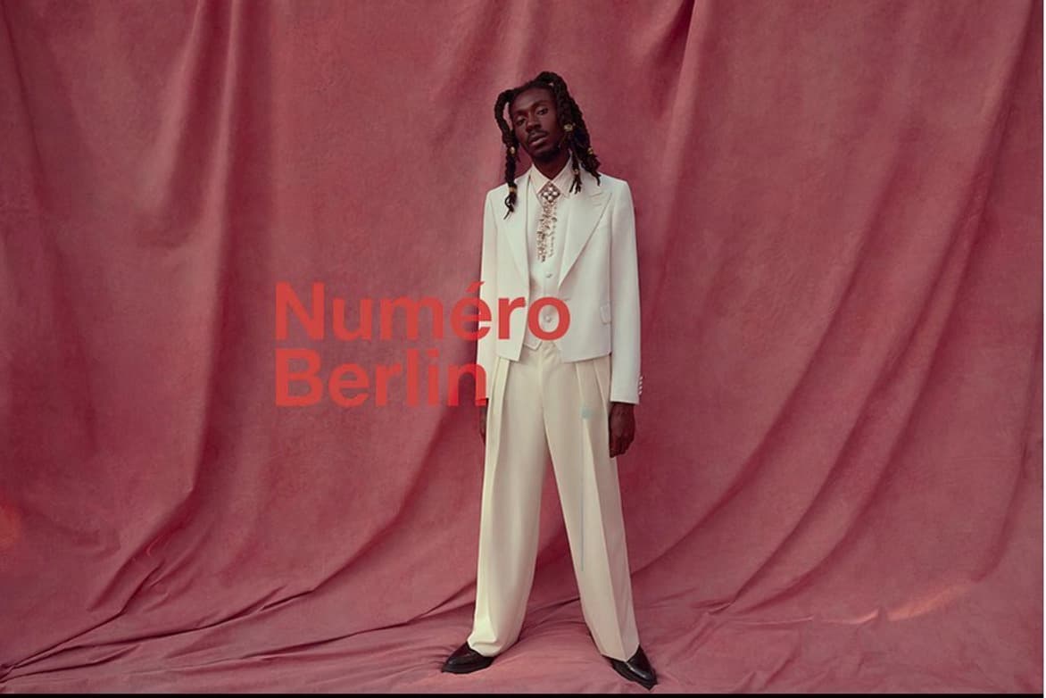 a man in a white suit standing in front of a red backdrop