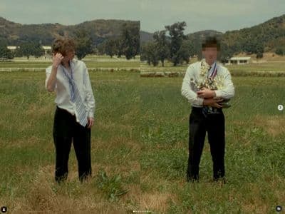 two men standing in a field with one talking on a cell phone