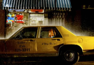 a yellow taxi cab driving down a rain soaked street