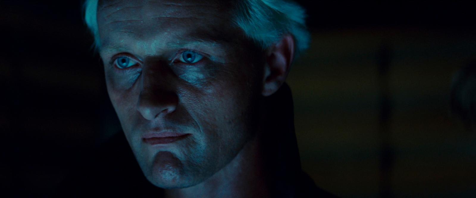 a man with white hair and blue eyes stares into the camera