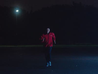 a man in a red jacket throwing a frisbee at night