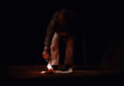 a man standing over a fire in the dark