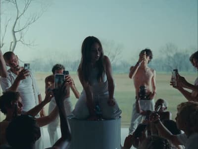 a woman sitting on top of a cake surrounded by people