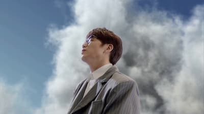 a man in a suit and tie standing in front of a cloudy sky