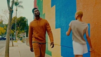 a man walking down a sidewalk next to a colorful wall