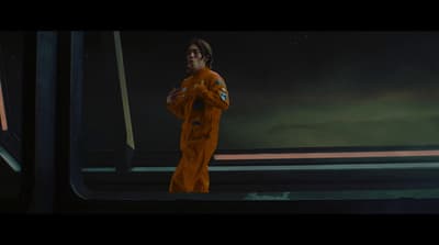 a man in an orange space suit standing in front of a window