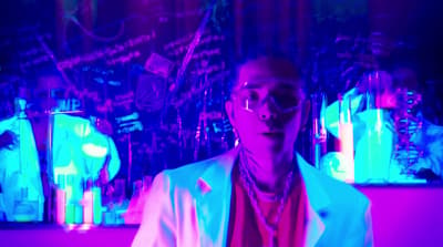 a man in a white jacket and glasses in a room with neon lights