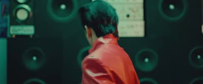 a man in a red jacket standing in front of a wall of speakers