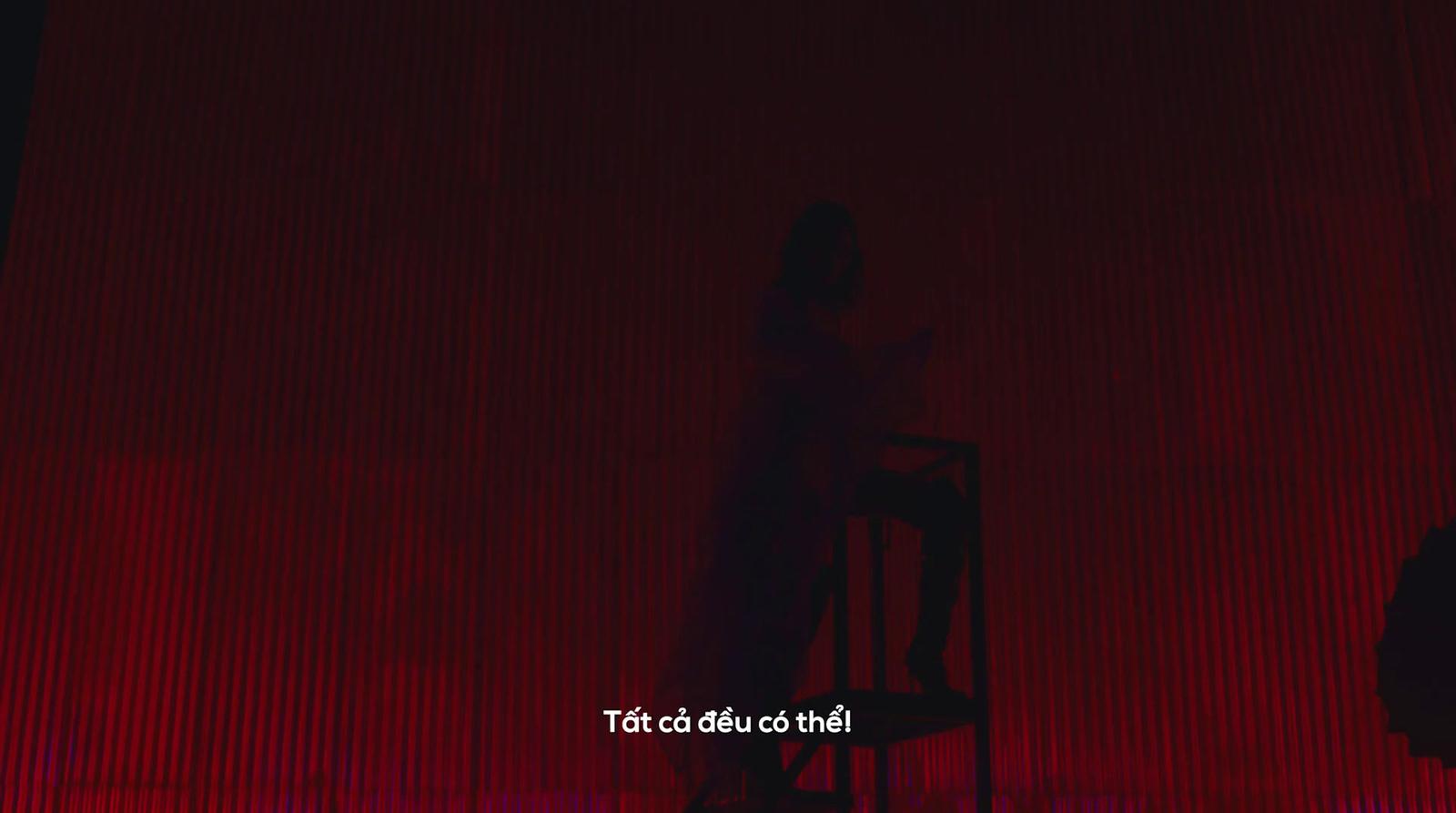 a person sitting on a chair in front of a red curtain