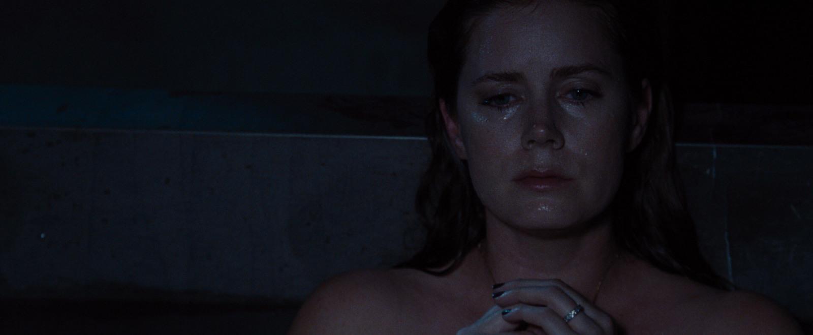 a shirtless woman holding a cigarette in a dark room