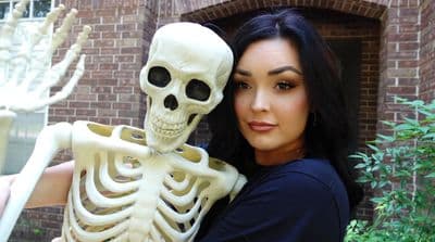 a woman holding a skeleton in front of a brick building