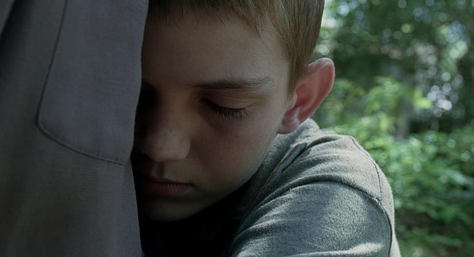 a young boy is holding his head against the back of a jacket