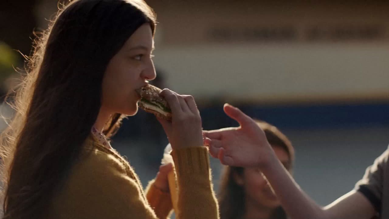 a woman eating a piece of food while standing next to a man