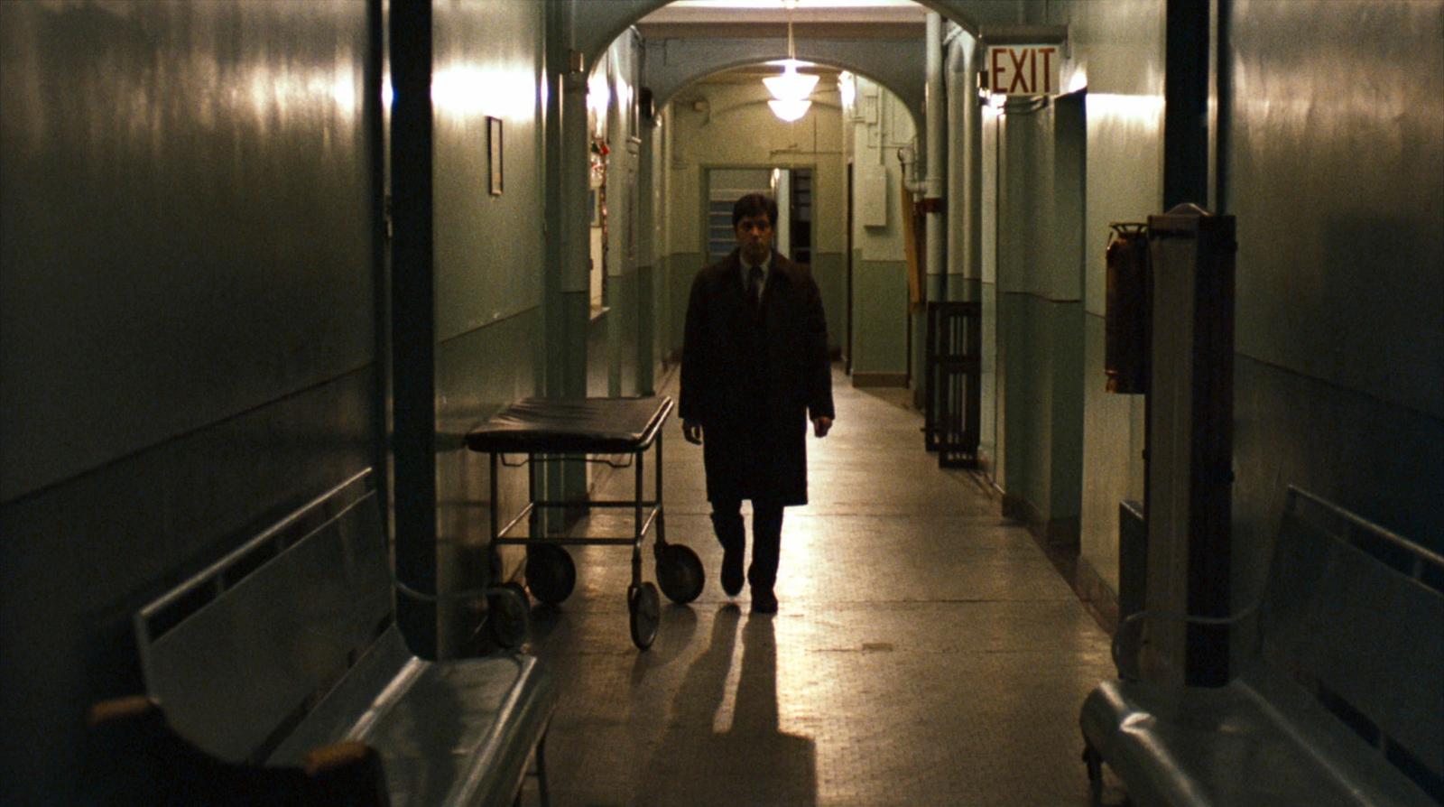 a man walking down a long hallway with a light on