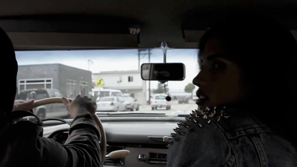 a woman driving a car with a man behind her