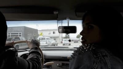 a woman driving a car with a man behind her