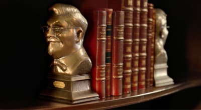 a bronze busturine of a man in front of a row of books