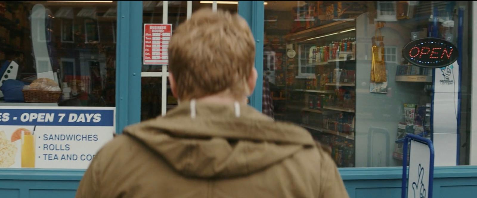 a man in a brown jacket walking past a store