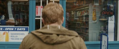 a man in a brown jacket walking past a store