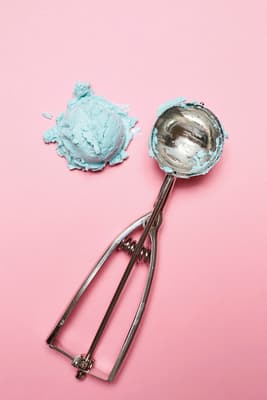 a scoop of blue paste next to a spoon on a pink background