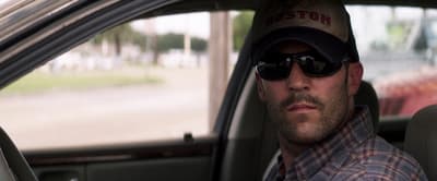 a man sitting in a car wearing a hat and sunglasses