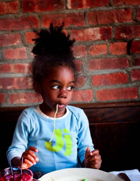 a little girl sitting at a table with a plate of food